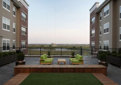 Outdoor courtyard at The Station at Lyndhurst Apartments featuring seating with cushions, wooden decking, and a well-maintained grass area.