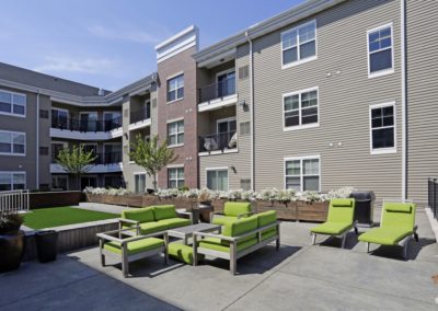 The outdoor courtyard at The Station at Lyndhurst Apartments featuring lounge seating with the apartment buildings with private balconies visible in the background.