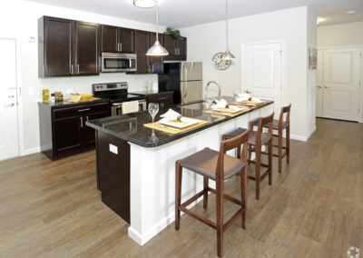 An open-concept kitchen at The Station at Lyndhurst Apartments featuring cabinetry, stainless steel appliances, and a countertop island with bar seating.