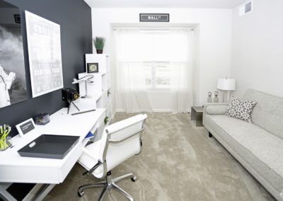 A home office space at The Station at Lyndhurst Apartments featuring a desk with a matching office chair, a black accent wall with framed artwork, and a sofa.
