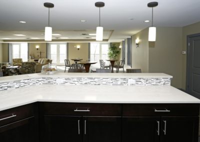 The community kitchen at The Station at Lyndhurst Apartments featuring countertops, cabinetry, and a mosaic tile backsplash. The lounge area with seating and dining tables is visible in the background.