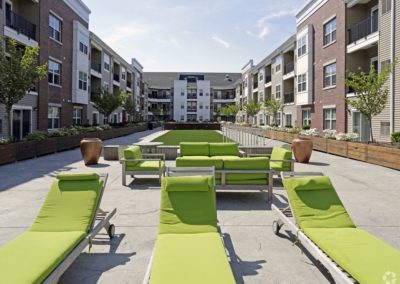 The outdoor courtyard at The Station at Lyndhurst Apartments featuring cushioned lounge chairs and sofas, surrounded by planters and the apartment buildings with balconies.